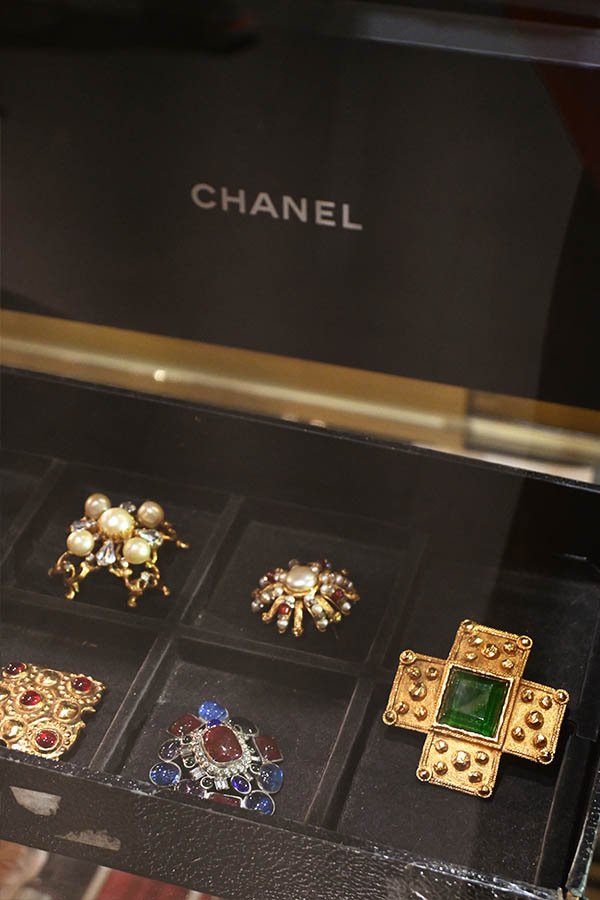 A-black-display-case-with-the-Chanel-logo-shows-several-vintage-style-brooches-and-pins-with-pearls-and-colorful-stones