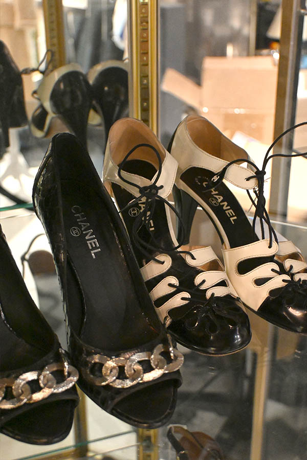 A-glass-display-case-shows-three-pairs-of-designer-shoes,-including-a-black-patent-leather-pump-with-a-gold-chain-detail-and-two-pairs-of-black-and-white-lace-up-heels,-all-bearing-the-Chanel-logo
