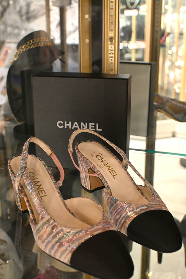 A-pair-of-Chanel-slingback-shoes-with-a-multi-colored-metallic-tweed-upper,-a-black-cap-toe,-and-a-textured-block-heel-is-displayed-in-front-of-a-black-Chanel-box