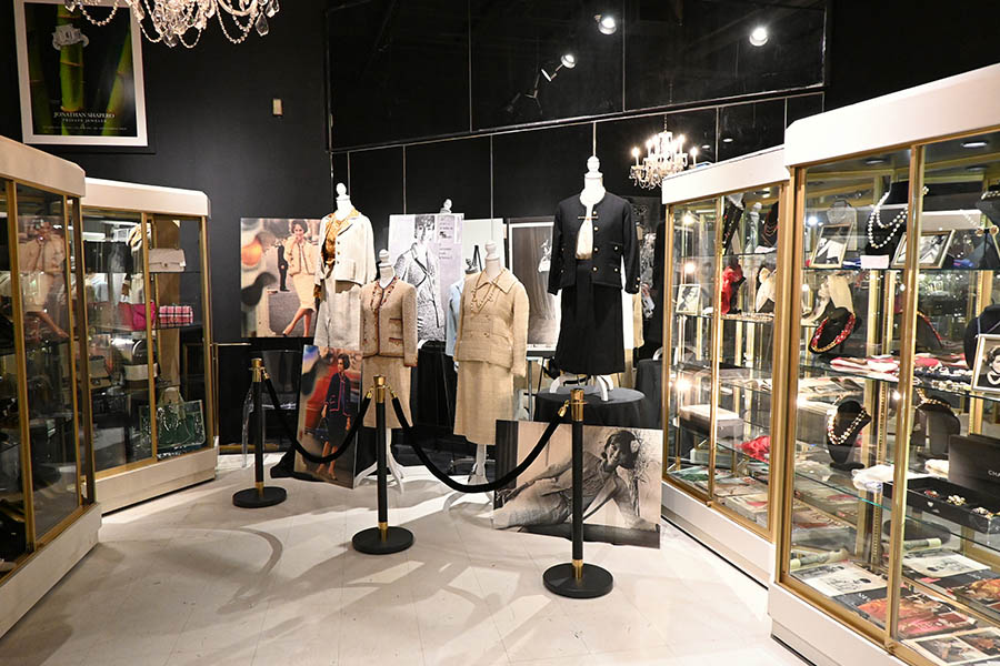 A-store-or-museum-exhibit-features-multiple-mannequins-wearing-Chanel-style-tweed-suits-and-multiple-glass-display-cases-filled-with-handbags-and-jewelry-including-necklaces-and-rings