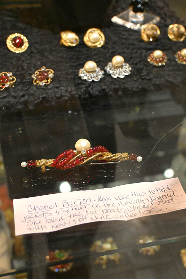 Chanel-bar-pin-made-of-twisted-gold-metal-and-woven-red-beads-with-a-large-central-pearl-is-displayed-in-a-glass-case