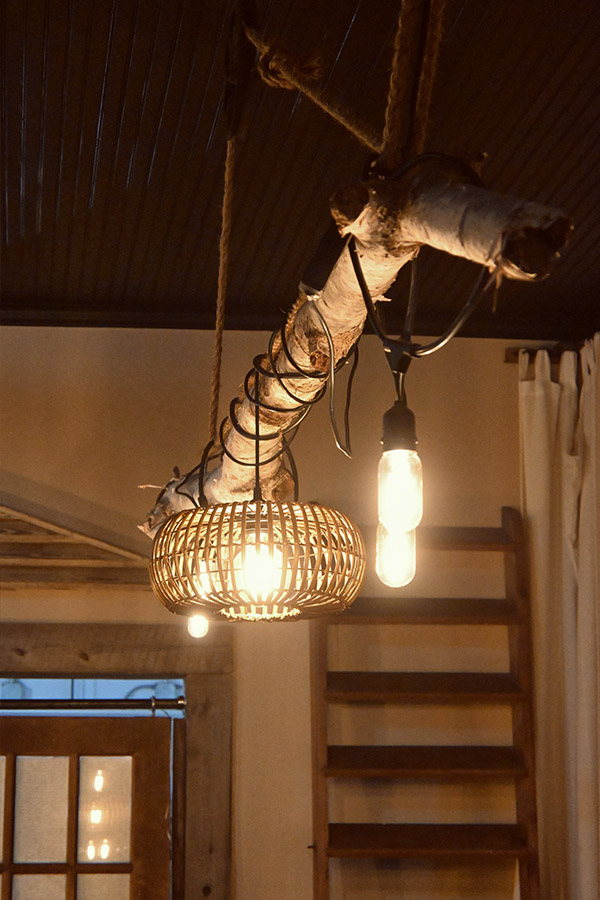 bohemian-design-style-light-fixture-made-from-a-twisted-piece-of-wood-with-a-wicker-or-rattan-shade-and-exposed-filament-lightbulbs