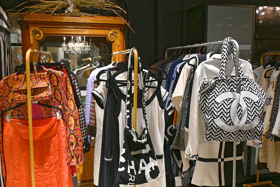 clothing-store-or-boutique-is-shown-with-a-mannequin-wearing-a-white-and-black-checkered-outfit-and-multiple-clothing-racks-with-a-prominent-black-and-white-bag-with-a-Chanel-style-logo