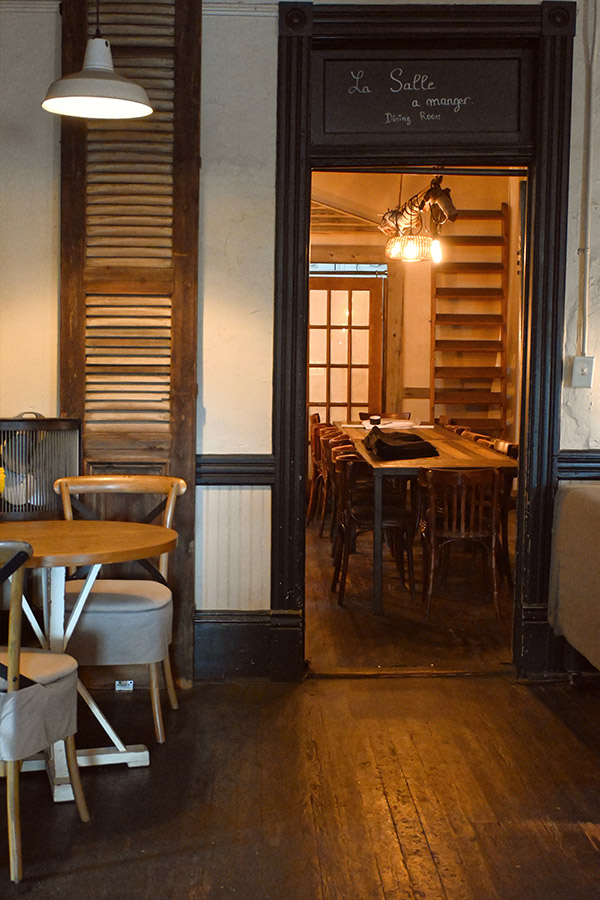 dark-wooden-doorway-leading-into-a-dining-room-with-long-wooden-tables-and-chairs-and-a-sign-above-the-door-reads-La-Salle-a-manger