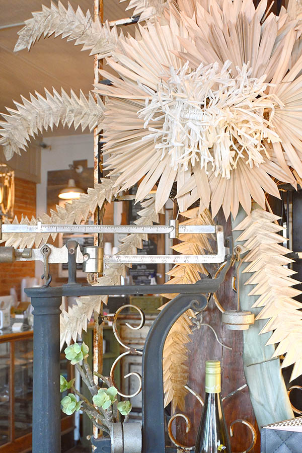 decorative-display-featuring-an-old-style-metal-scale-in-the-center-surrounded-by-large-dried-palm-fronds-or-botanical-decorations-made-of-paper