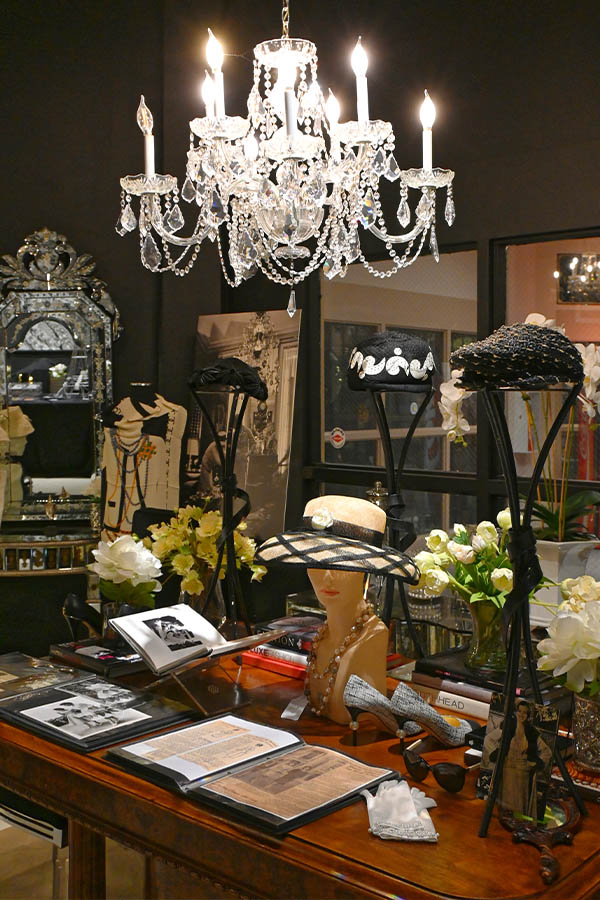 display-in-a-store-or-museum-is-shown-with-a-crystal-chandelier-hanging-over-a-wooden-table-with-multiple-hats,-books,-and-accessories-on-display