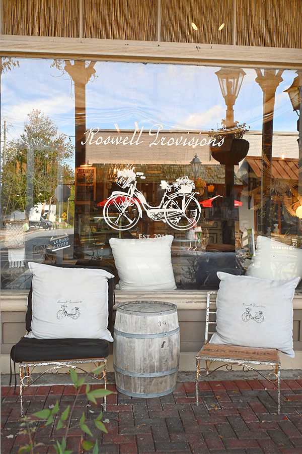 french-decor-style-storefront-of-a-shop-called-Roswell-Provisions-featuring-a-large-window-with-a-white-bicycle-decal-on-it
