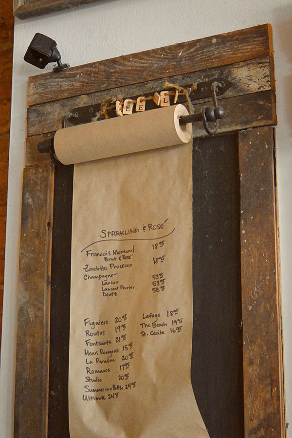 french-design-handwritten-menu-for-sparkling-and-rosé-wines-with-their-prices-on-a-roll-of-brown-paper-mounted-on-a-rustic-wooden-board