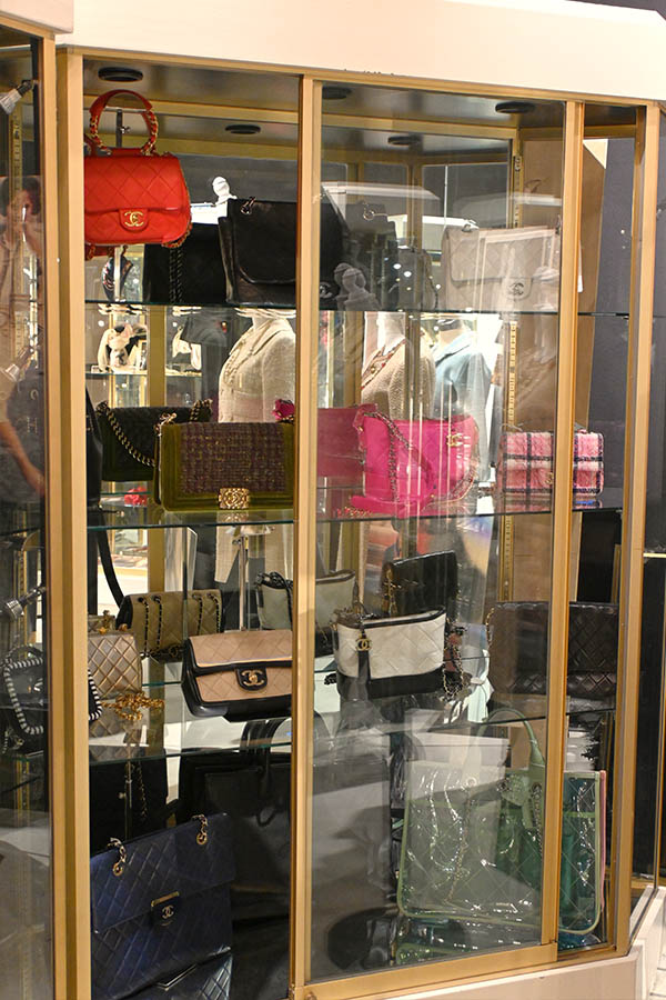 glass-display-case-shows-multiple-Chanel-designer-handbags-on-four-shelves-including-red-quilted-and-black-leather-bags