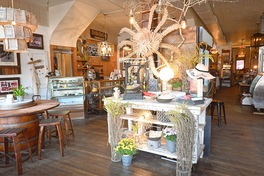 interior-of-Roswell-Provisions-with-a-rustic-and-French-Provincial-design-style-that-features-a-white-wooden-display-table-with-various-decorative-items-and-a-large-wooden-sculpture