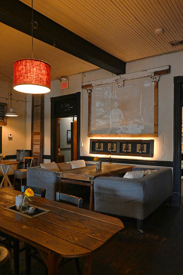 interior-space-with-two-long-wooden-tables-in-the-foreground-and-a-seating-area-with-a-wooden-table-and-two-gray-couches-in-the-background