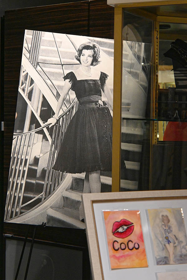 large-black-and-white-photograph-of-a-woman-in-a-black-dress-and-pearl-necklace-on-a-spiral-staircase-is-shown-in-a-display