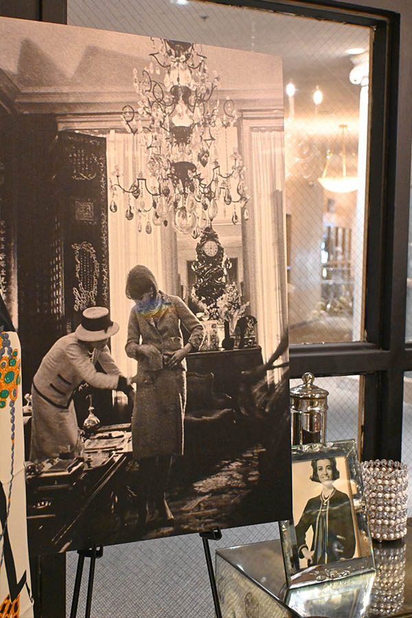 large-black-and-white-photograph-on-an-easel-depicts-two-women-in-Chanel-style-suits-in-an-ornate-room-with-a-chandelier-and-antique-furniture-photo-and-a-pearl-covered-container