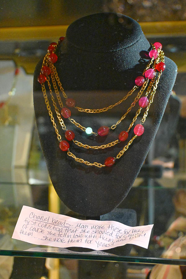 multi-strand-necklace-with-gold-tone-chains-and-red-beads-is-displayed-on-a-black-bust-with-a-handwritten-note-in-the-foreground