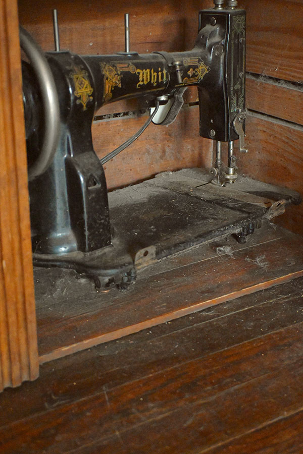 old-black-sewing-machine-with-gold-filigree-designs-and-the-name-WHIT-on-it-which-is-partially-recessed-into-a-wooden-cabinet