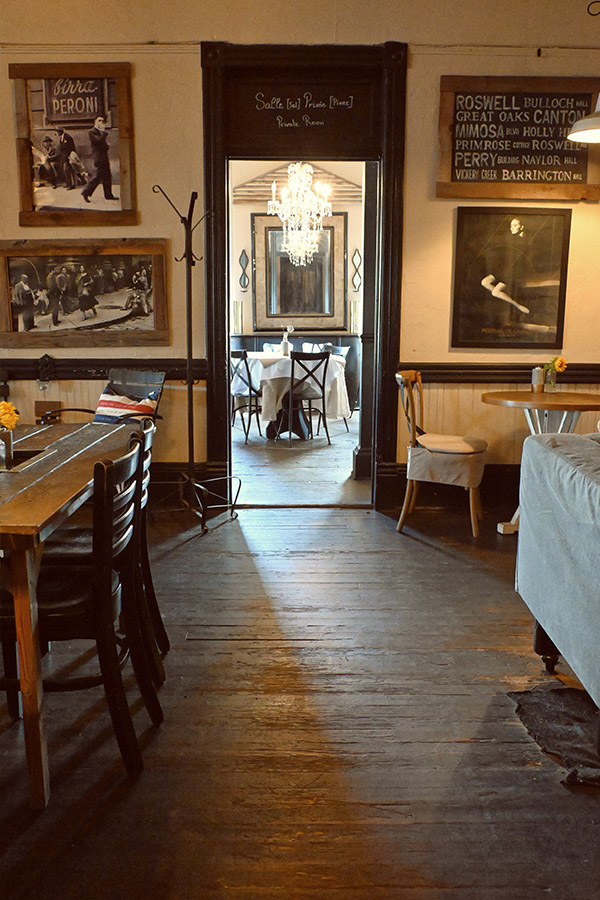 rustic-and-vintage-design-style-of-a-restaurant-interior-with-a-worn-wooden-floor-a-long-dining-table-and-a-couch-with-a-round-table-in-the-foreground-and-a-doorway