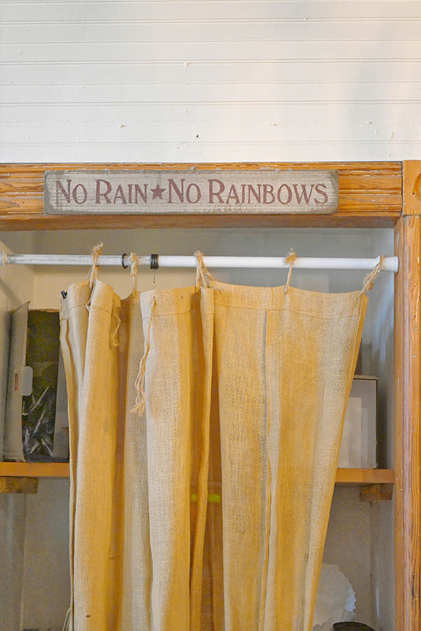 rustic-wooden-sign-with-the-phrase-NO-RAIN-NO-RAINBOWS-hanging-on-a-wooden-shelf