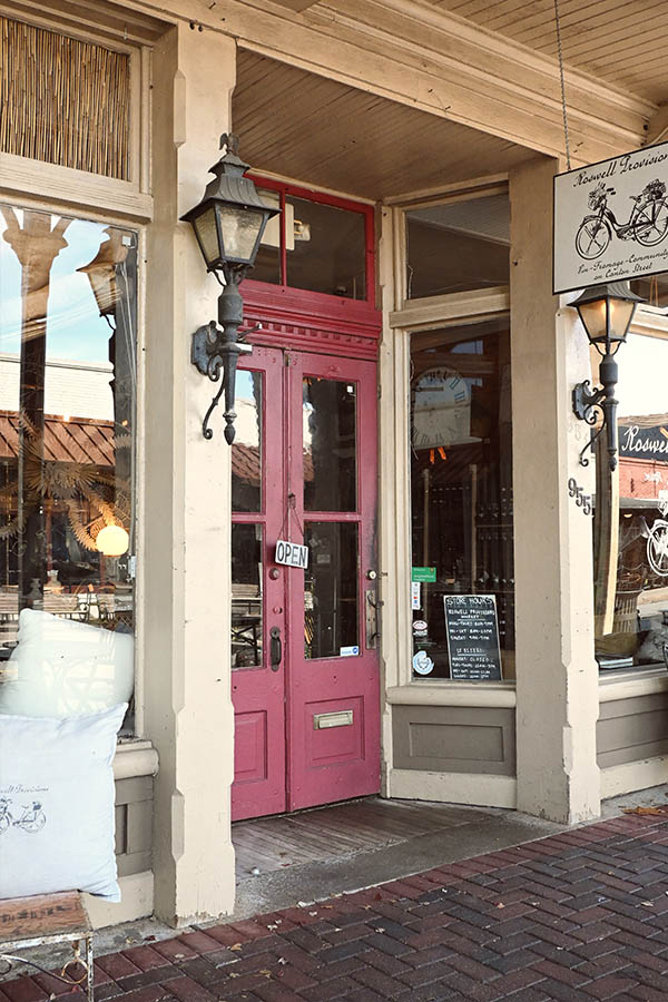 street-level-photo-of-the-exterior-of-a-shop-called-Roswell-Provisions-which-features-a-bright-red-double-door-with-an-open-sign-and-two-black-vintage-style-lanterns