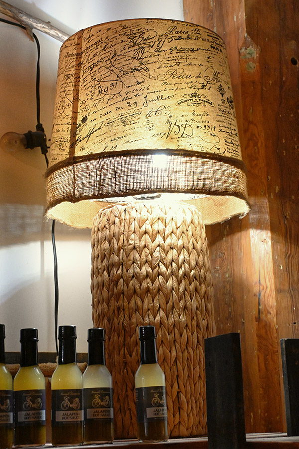table-lamp-with-a-woven-wicker-or-rattan-base-and-a-lampshade-with-a-printed-parchment-like-pattern-of-French-writing-and-a-burlap-trim