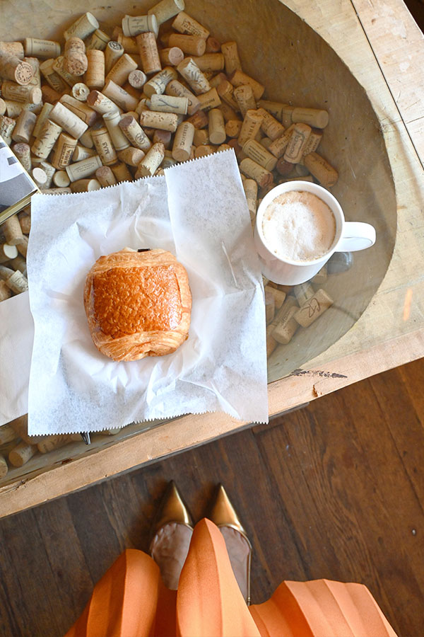 table-setting-with-a-freshly-baked-pain-au-chocolat-pastry-on-a-white-paper-napkin-next-to-a-white-mug-filled-with-a-cappuccino-or-latte