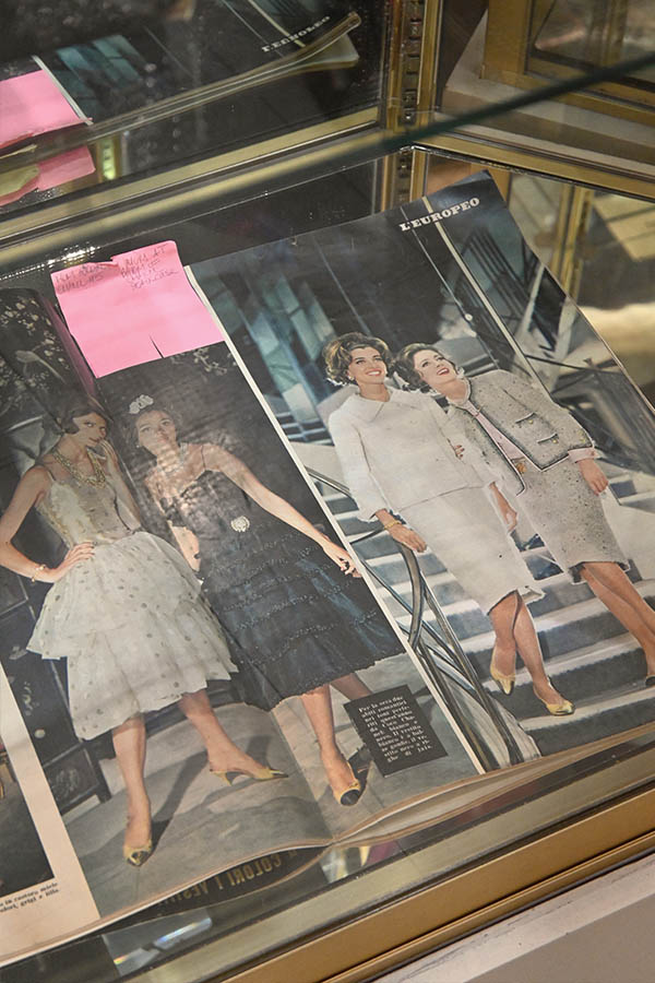 vintage-magazine-spread-is-displayed-in-a-glass-case,-showing-black-and-white-photos-of-women-in-1960s-fashion-including-cocktail-dresses-and-tweed-suits