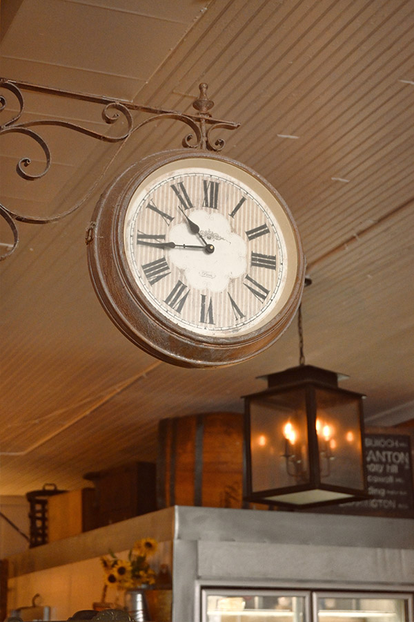 vintage-style-double-sided-clock-with-a-brown-frame-and-Roman-numerals-that-is-hanging-from-a-wrought-iron-scroll-bracket