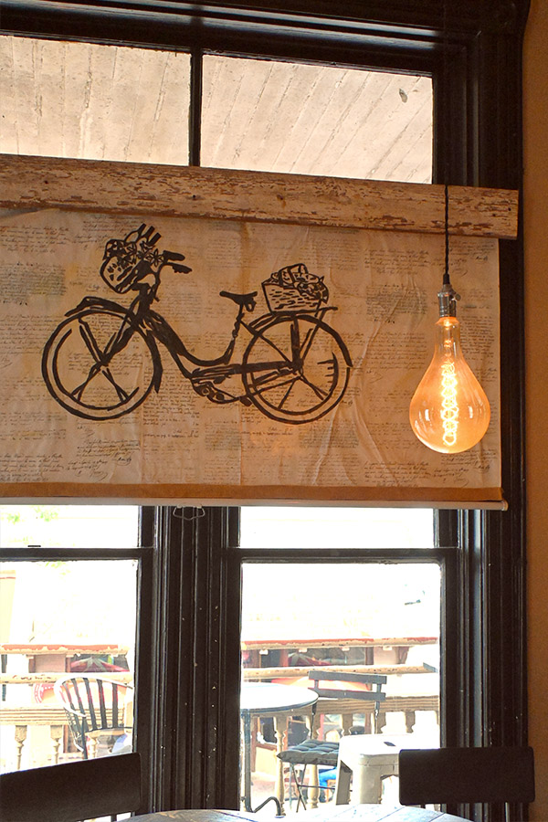 window-with-a-roller-shade-that-has-a-black-bicycle-illustration-on-it-and-a-large-exposed-filament-lightbulb-hanging-from-the-ceiling