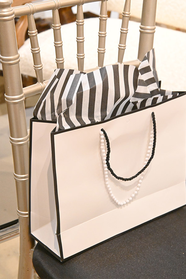 white-gift-bag-with-black-and-white-striped-tissue-paper-and-pearl-necklace-on-gold-chair