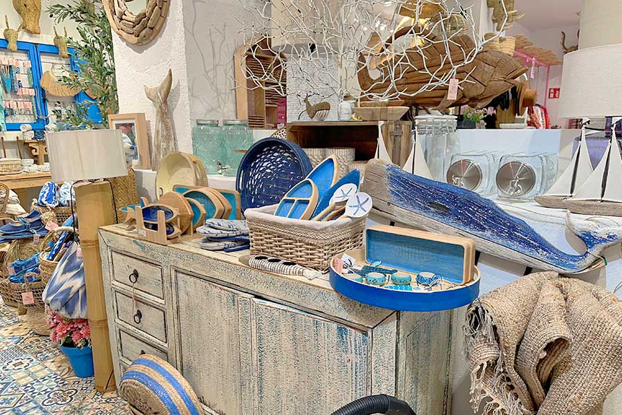 Coastal-themed-retail-display-featuring-a-distressed-white-wooden-sideboard-adorned-with-blue-nautical-decor-including-wooden-fish-sculptures-sailboat