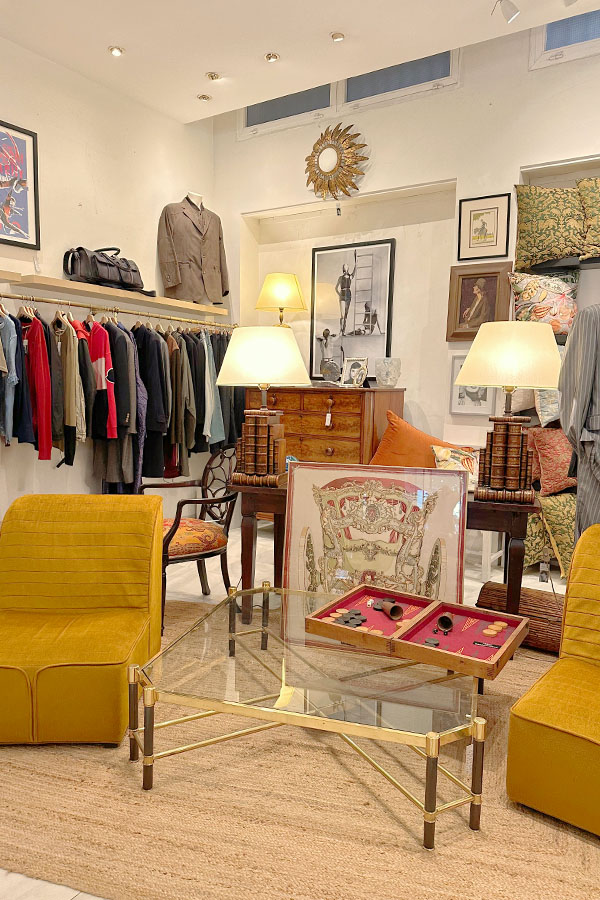 Eclectic-vintage-style-boutique-featuring-mustard-yellow-velvet-chairs-a-glass-and-brass-coffee-table-and-a-curated-selection-of-clothing-hanging-from-a-wooden-shelf