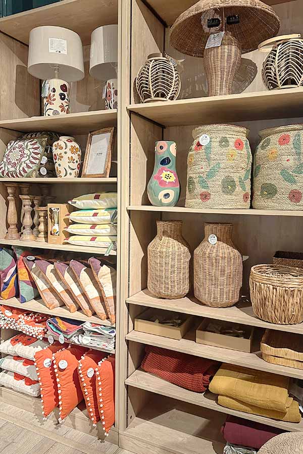 Light-wood-shelving-unit-filled-with-an-array-of-home-decor-items-including-woven-wicker-lanterns-black-and-white-striped-vases