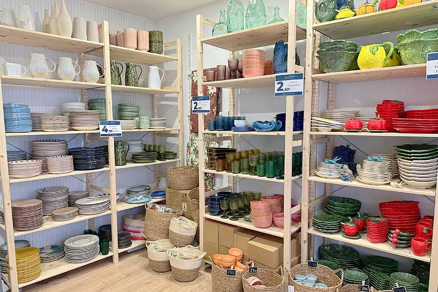Wooden-shelving-displaying-a-wide-variety-of-colorful-ceramic-tableware-including-green-cabbage-shaped-bowls-red-strawberry-plates