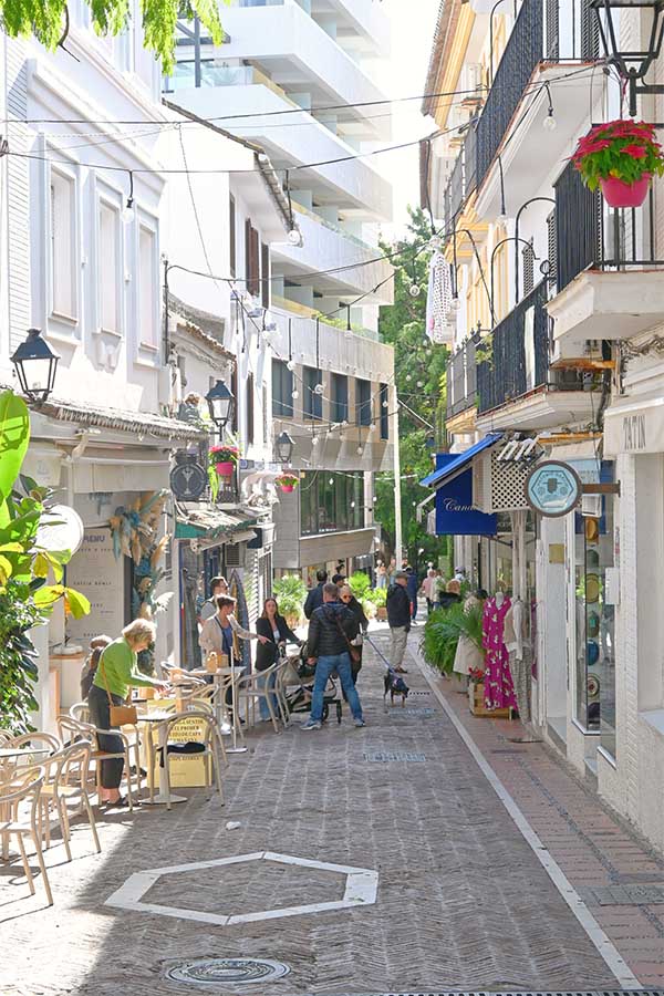 bustling-narrow-shopping-street-lined-with-white-buildings-features-outdoor-cafe