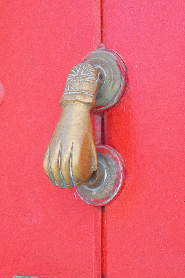 door-knocker-shaped-like-a-clenched-human-hand-is-mounted-on-a-bright-red-wooden-door-surface