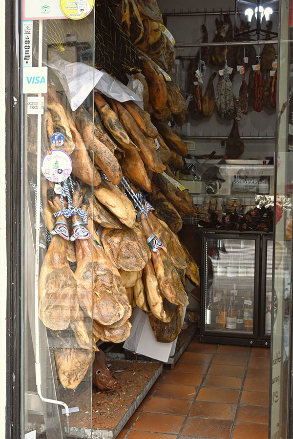 many-cured-ham-legs-known-as-jamon-hanging-densely-from-the-ceiling-and-displayed-behind-a-glass-door