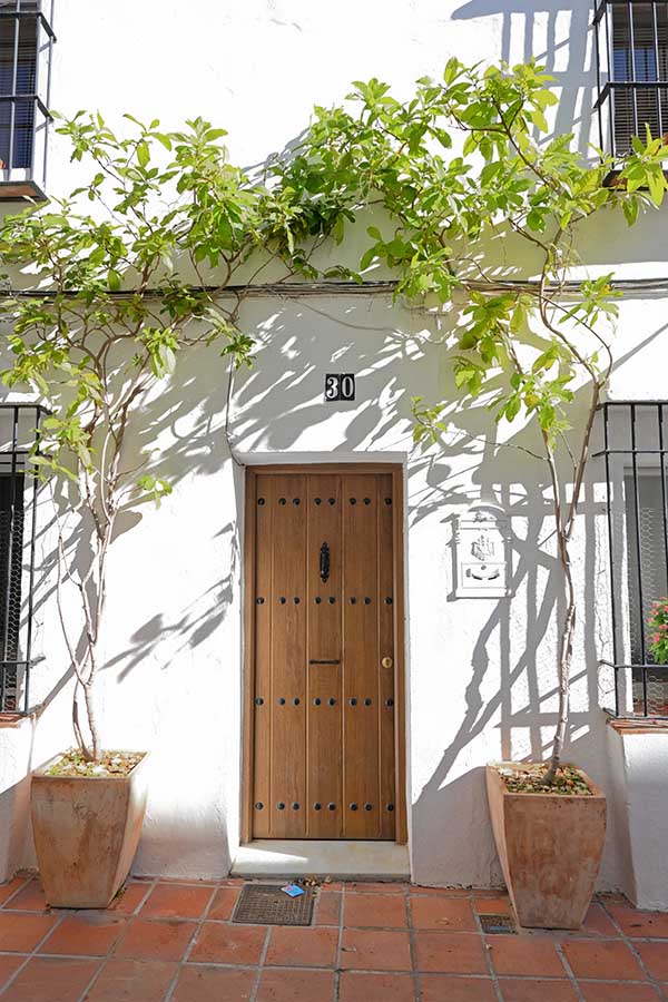 medium-toned-wooden-door-with-black-circular-studs-stands-centered-on-a-white-textured-wall