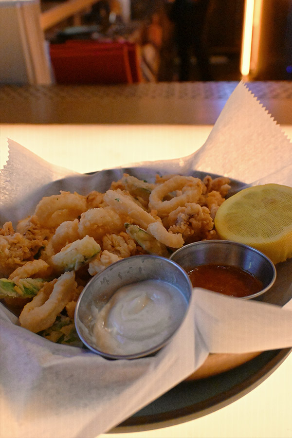 plate-of-crispy-fried-calamari-and-zucchini-is-served-on-white-parchment-paper-with-two-small-metal-containers-of-dipping-sauce