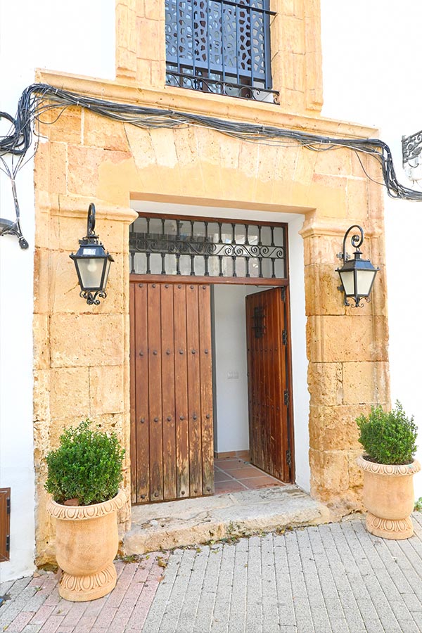 stone-archway-with-two-black-lanterns-and-an-open-wooden-door-is-flanked-by-two-large-ornate-terracotta-planters