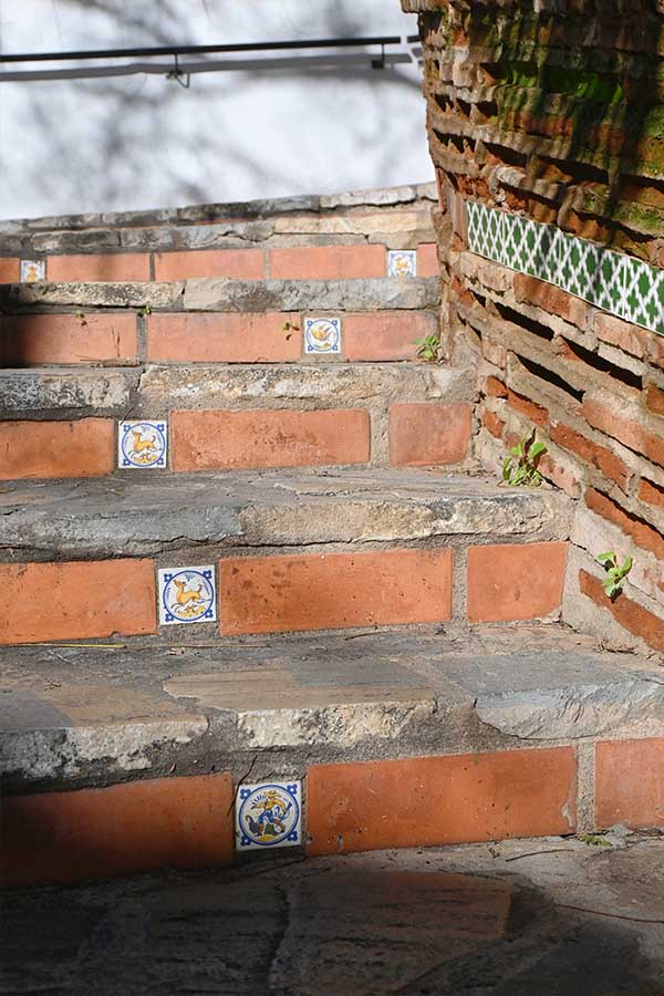 stone-stairs-with-terracotta-brick-risers-feature-small-blue-and-yellow-decorative-tiles-embedded-at-intervals
