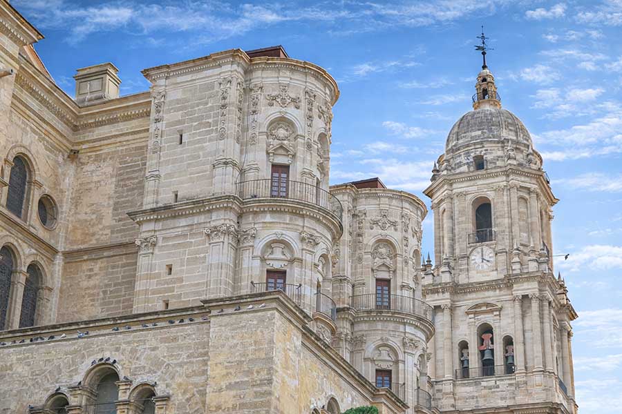 Grand-stone-cathedral-featuring-ornate-Renaissance-towers-and-a-bell-tower-against-a-cloudy-blue-sky-malaga
