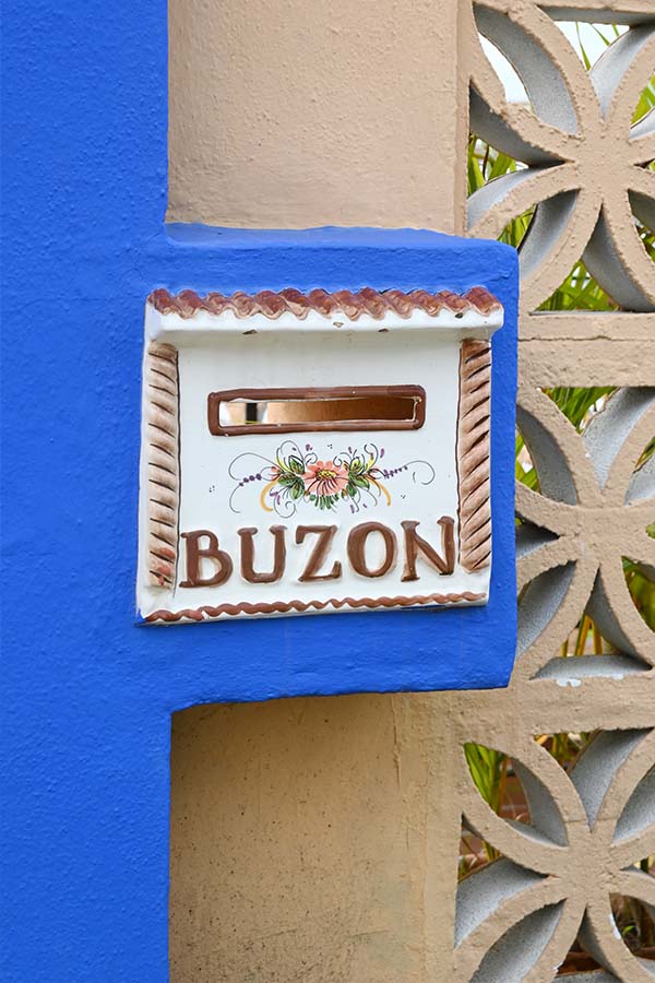 Hand-painted-ceramic-mailbox-with-the-word-BUZON-mounted-on-a-vibrant-blue-and-tan-wall