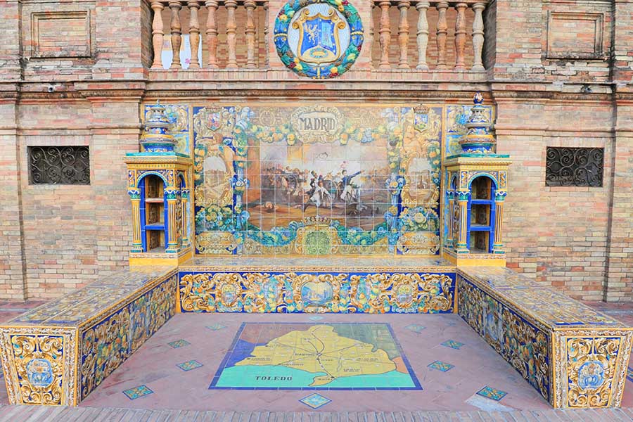 Ornate-ceramic-fountain-and-tiled-mural-set-into-a-brick-wall-with-a-balustrade-above