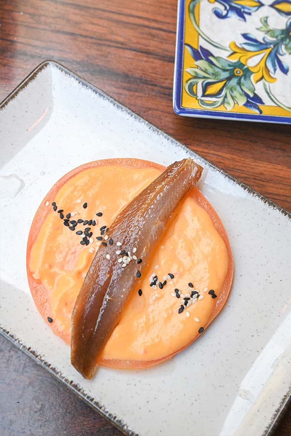 Single-anchovy-fillet-atop-a-round-slice-of-tomato-spread-with-orange-sauce-spanish-food