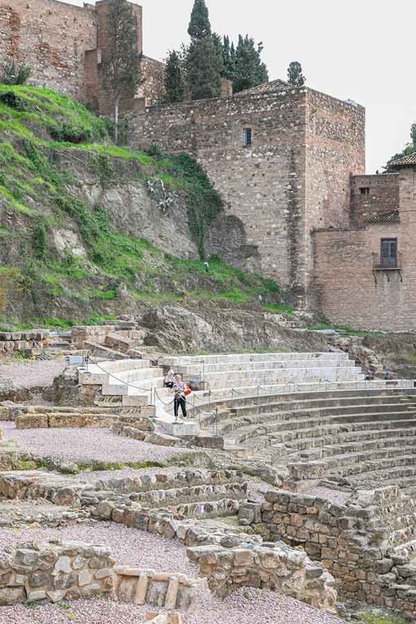 Stone-amphitheater-ruins-nestled-against-a-rocky-hillside-with-ancient-fortress