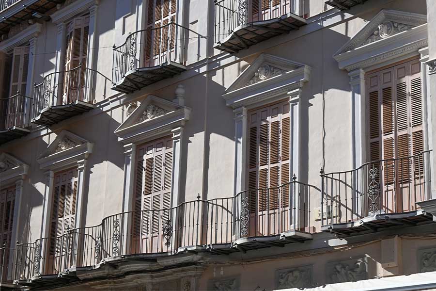Sunlit-building-facade-with-classical-balconies-wrought-iron-railings-and-wooden-shutters