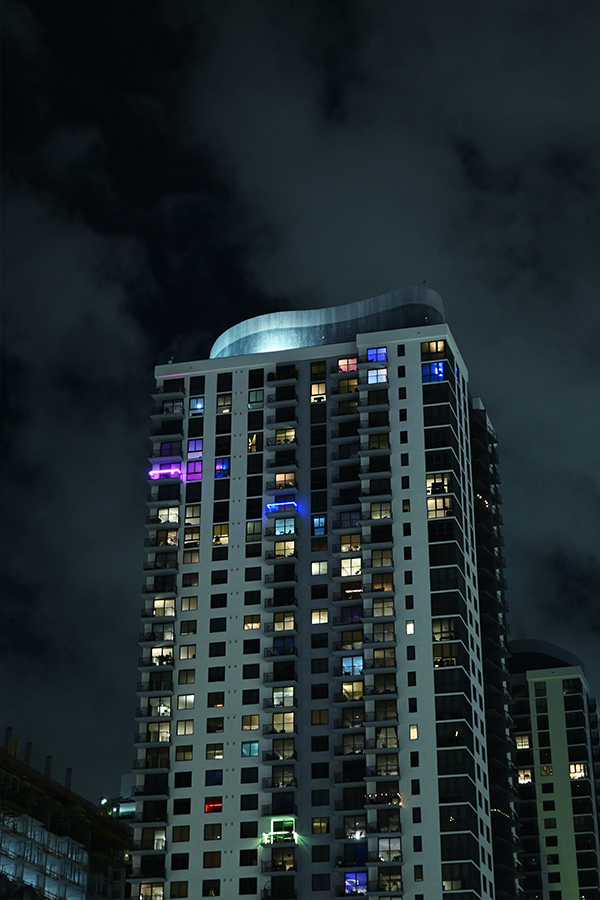 towering-white-residential-building-with-sporadic-colored-balcony-lights-piercing-the-Miami-architecture-night