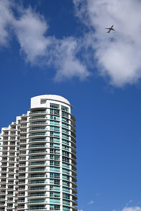 white-balconies-of-a-Miami-architecture-high-rise-against-a-bright-blue-sky-with-a-passing-airplane