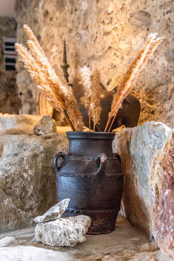 earth-toned-ceramic-urn-with-dried-pampas-grass-against-stone-wall-showing-castle-design