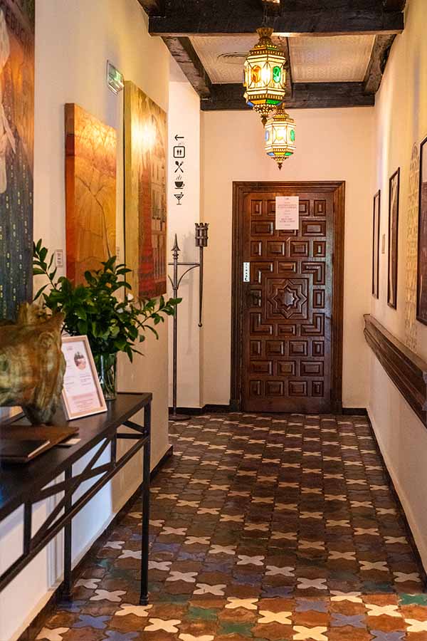 long-hallway-with-patterned-tile-flooring-hanging-lanterns-and-wooden-door-displaying-traditional-castle-design