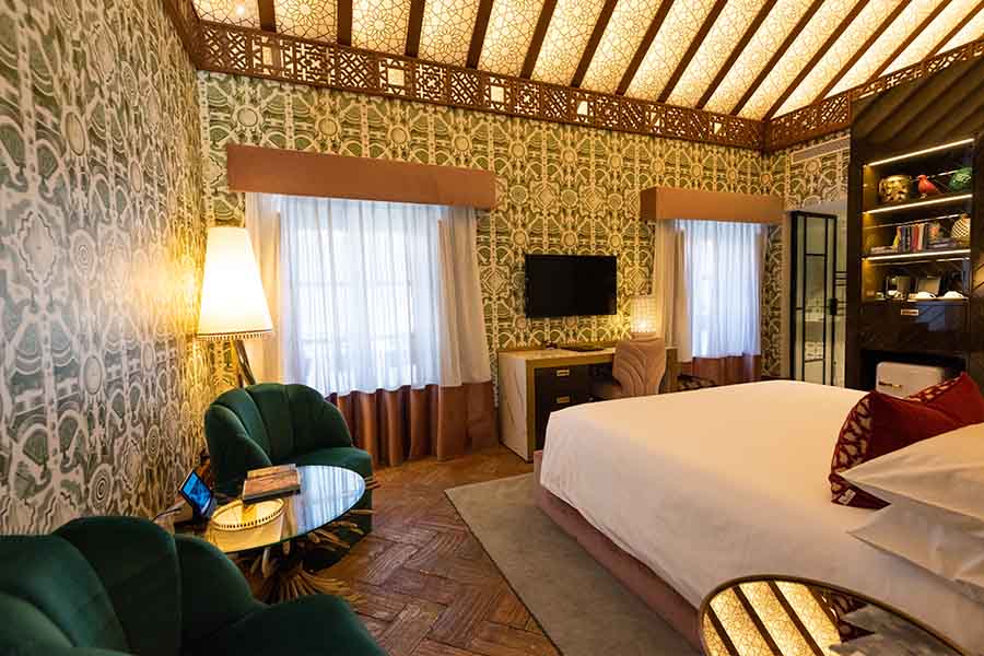 Spacious-hotel-room-king-bed-green-armchairs-patterned-wallpaper-hotel-claude-marbella-spain-interior-design-boutique-hotel-design